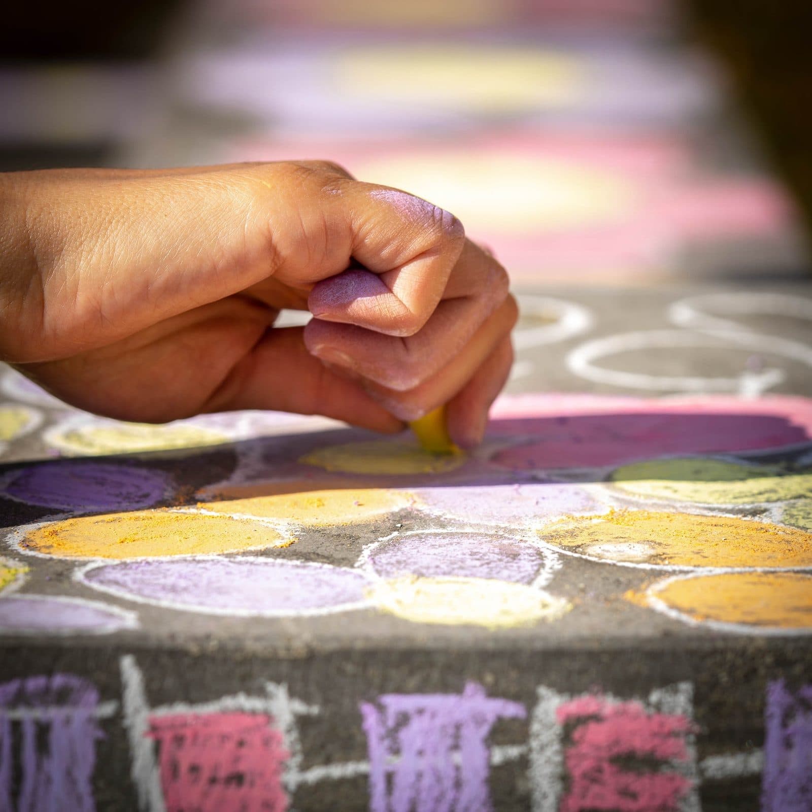 A hand drawing a coloured chalk mandala on the ground