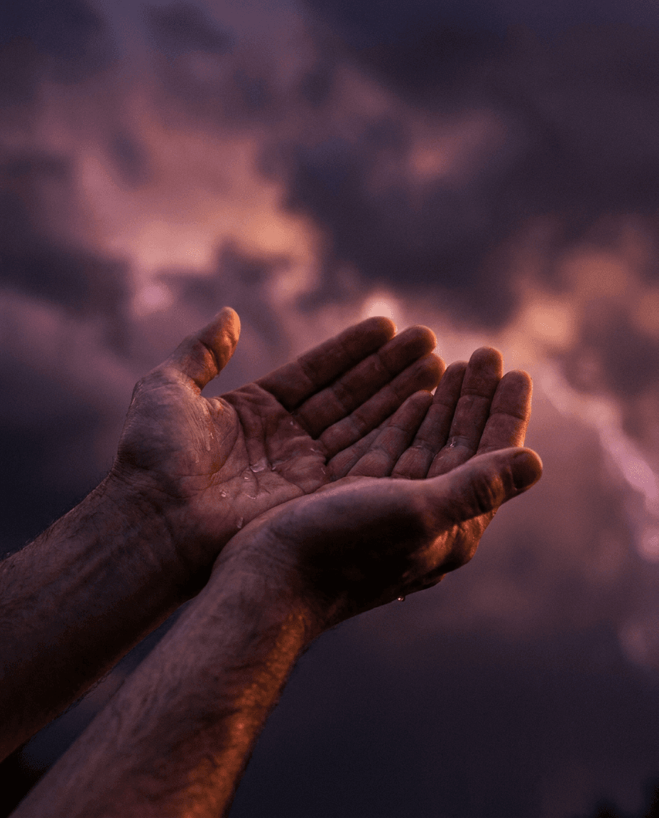 Open hands catching rain under a storm sky